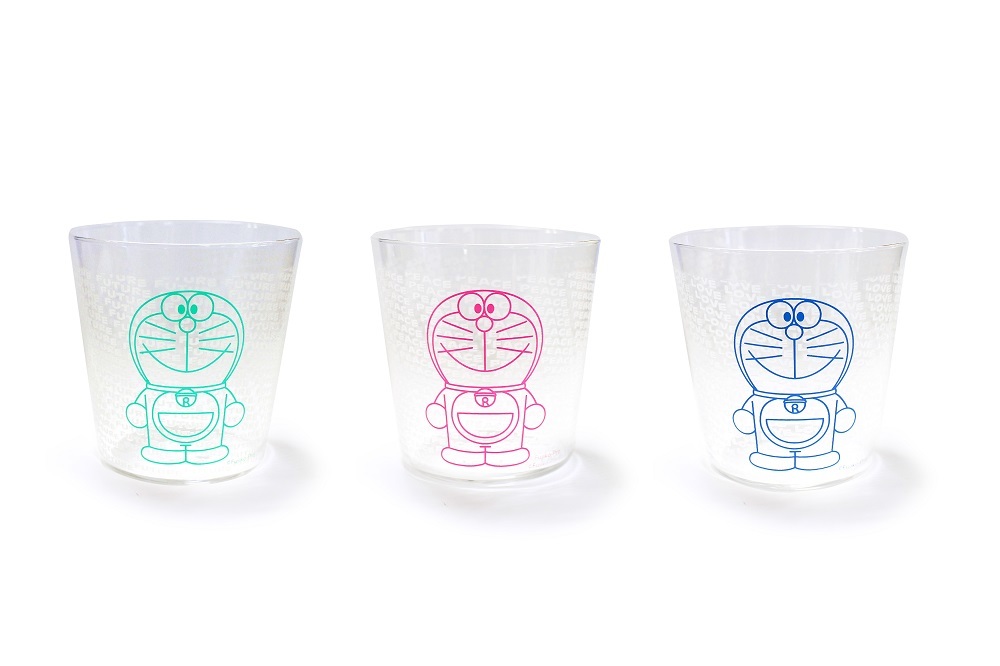 カラーチェンジグラス - 全3種-（各1,512円）　©Fujiko-Pro 微笑むドラえもんをデザインしたグラス。 冷たい飲料をグラスに入れると、それぞれ文字が浮かび上がる。