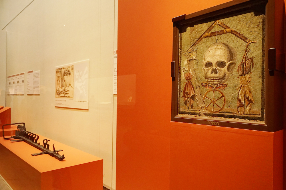 左奥：《奴隷の拘束具》鉄　右手前：《テーブル天板 通称「メメント・モリ」》モザイク、ともにナポリ国立考古学博物館蔵