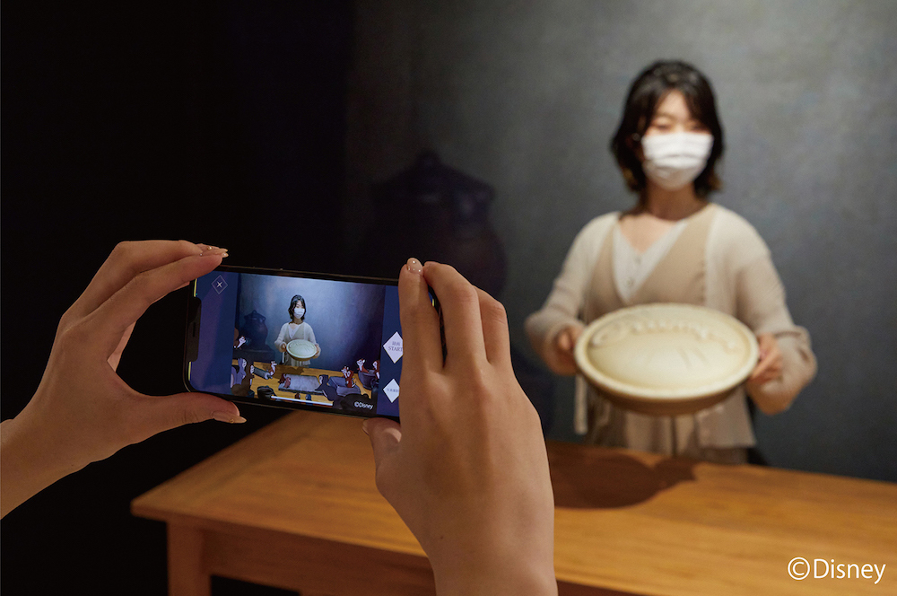 『白雪姫』より　パイを手にもってスマートフォンをかざすと、そこはこびとたちの家。白雪姫のように、森の動物たちと一緒にパイをつくりましょう。