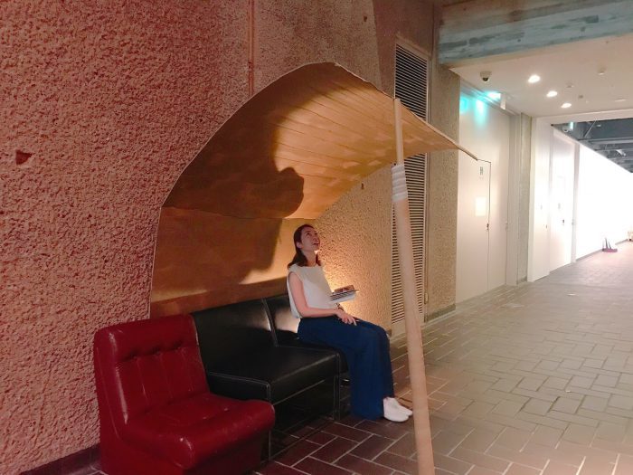 吹き抜けの展示室に抜ける途中には、本展準備を手伝った東京藝術大学の学生が日頃使っているソファと、この空間に合わせてつくった屋根が。 座って見るのも楽しい。ひさしの形は展示室の天井のアーチの形と呼応している。