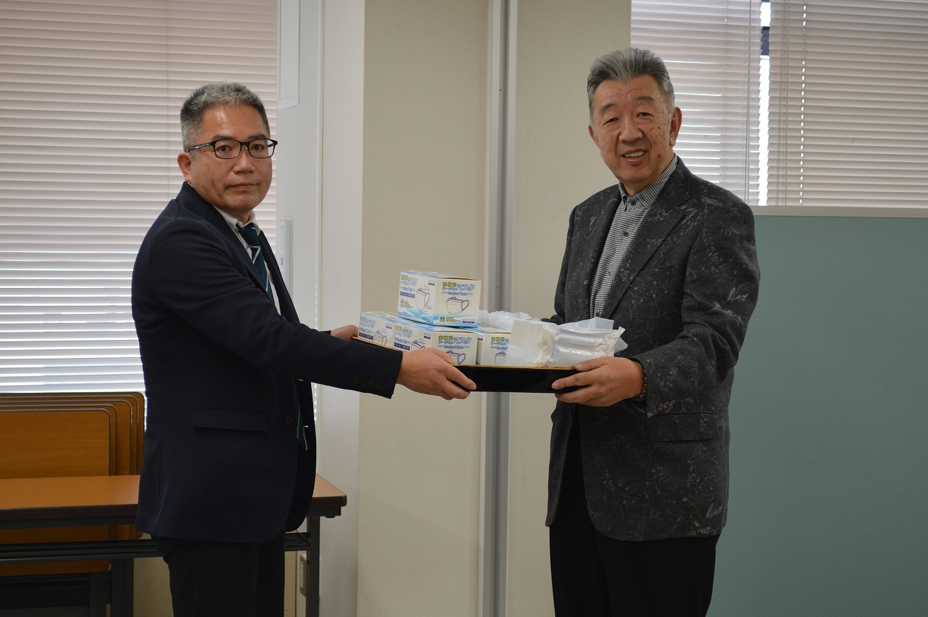 初代タイガーマスク後援会の大倉満理事長（写真右）から社会福祉法人東京都社会福祉協議会乳児部会部会長の都留和光氏（写真左）へ、１万枚のマスクが手渡された