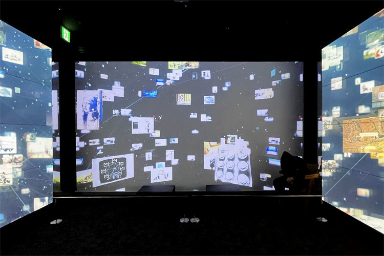 『バンクシー展』会場風景。三面スクリーンの映像でバンクシーの世界に没入。 正面スクリーン右下にはバンクシーらしき人物が……。
