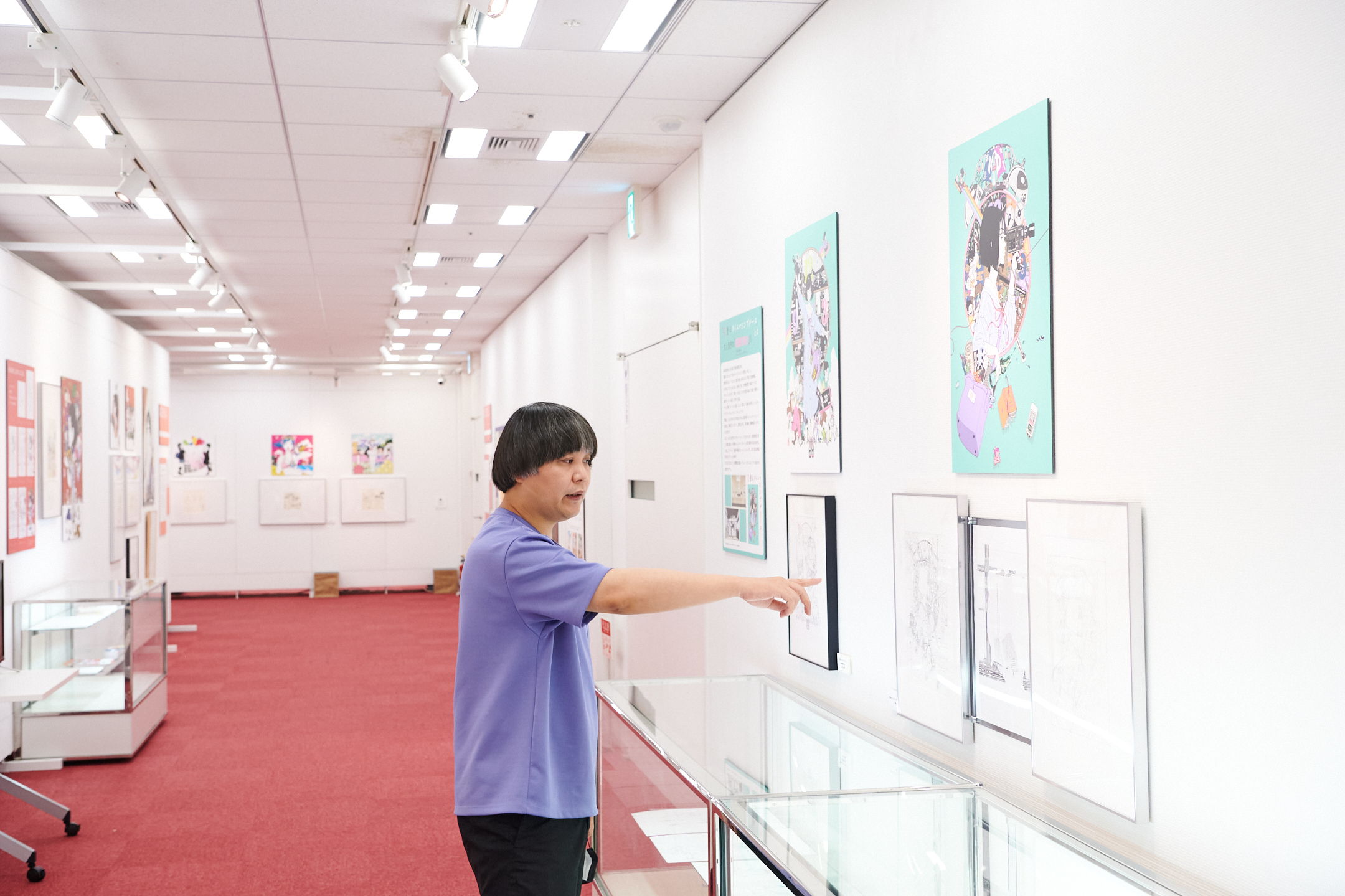 展示会場で前回から増えた展示物を指差す中村佑介