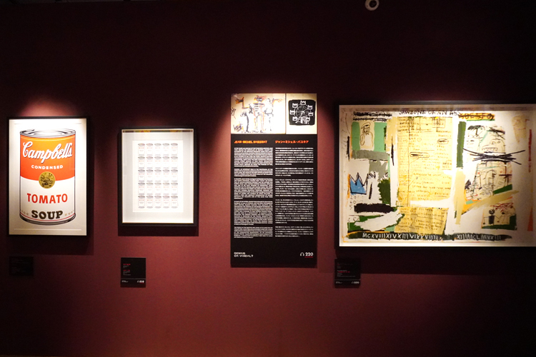 『バンクシー展　天才か反逆者か』展示風景。左より：アンディ・ウォーホル《キャンベルのスープ缶　トマト・スープ　サンデー・B・モーニング・エディション》、バンクシー《スープ・カンス》、ジャン＝ミシェル・バスキア《ジョウボーン・オブ・アン・アス》