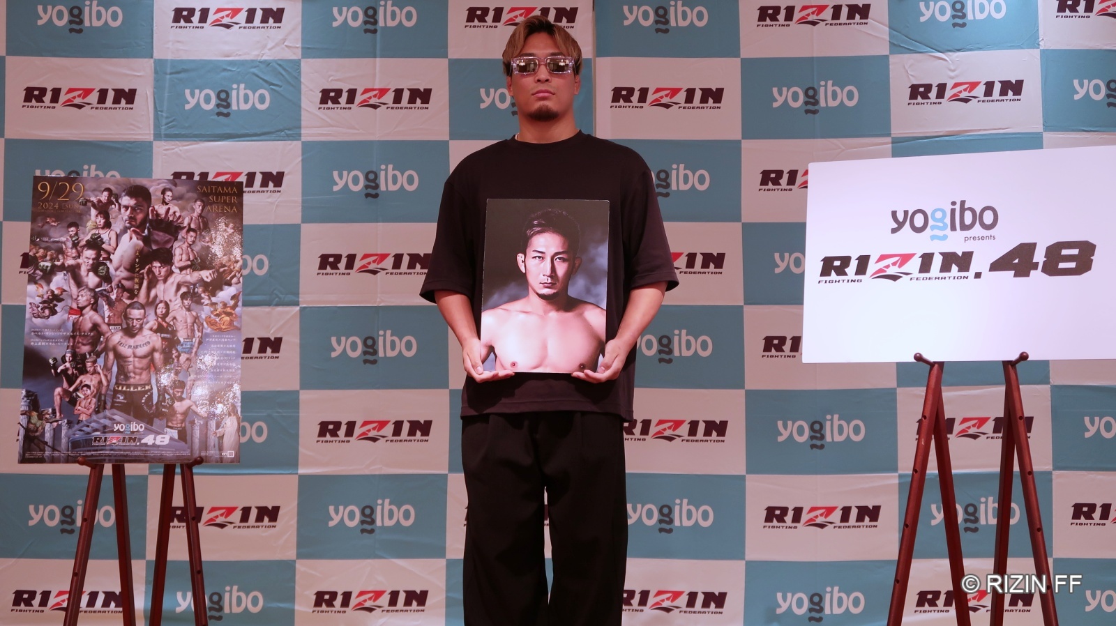 会見で元谷の写真を手に勝利を誓う太田忍