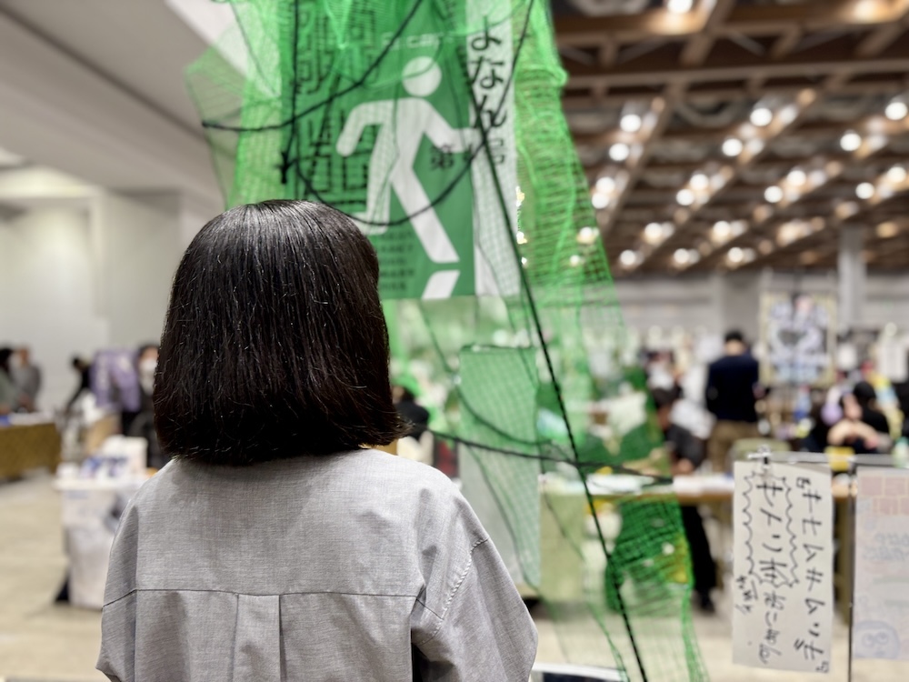 あっ、網で前よく見えない……（ブースに立つ仲間のT女史）