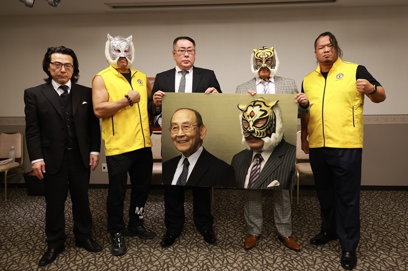 新間寿氏と佐山サトル総監のボードを手にした選手、大会関係者ら