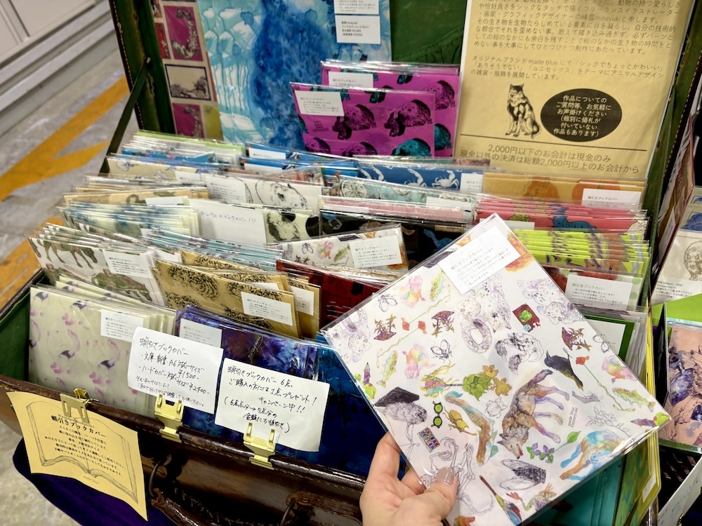 イラストレーター・画家・グラフィックデザイナーの峰雪さんのブース「made blue」にて（カテゴリは小説／短編・掌編・ショートショート）。筆者は25種の動植物をデザインした博物柄のカバーを購入！